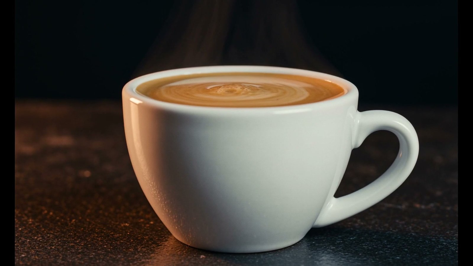 A full cup of espresso with settled golden crema on a dark counter, steam rising